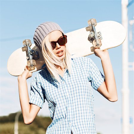 simsearch:400-07506274,k - Close-up of young blond girl in beanie hat and leopard sunglasses who stands near granite fence on sunny day holding skateboard on her shoulders Fotografie stock - Microstock e Abbonamento, Codice: 400-07509953