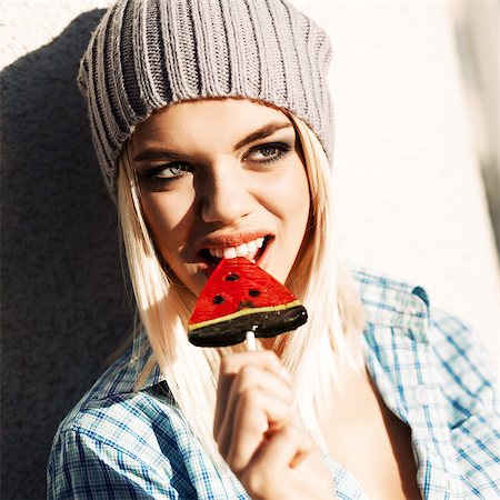 simsearch:400-07506274,k - Portrait of beautiful smiling blond girl who bites sweet bright watermelon lollipop with healthy white teeth Fotografie stock - Microstock e Abbonamento, Codice: 400-07509967