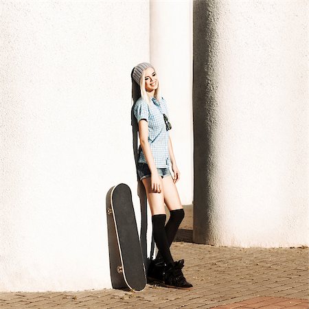 Happy smiling girl in short shorts and stockings with skateboard stands by columns on sunny day Stock Photo - Budget Royalty-Free & Subscription, Code: 400-07509960