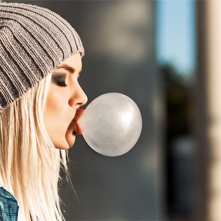 simsearch:400-07506274,k - Portrait of beautiful young blonde teenage girl in beanie hat blows big bubble from bubble gum Fotografie stock - Microstock e Abbonamento, Codice: 400-07509970