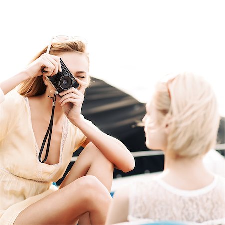 beautiful girl with camera in yellow summer dress takes picture of her blonde girlfriend against water Foto de stock - Super Valor sin royalties y Suscripción, Código: 400-07509982