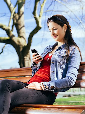 Photo of a beautiful young woman using a smartphone while sitting in a park on a bench. Stock Photo - Budget Royalty-Free & Subscription, Code: 400-07503278