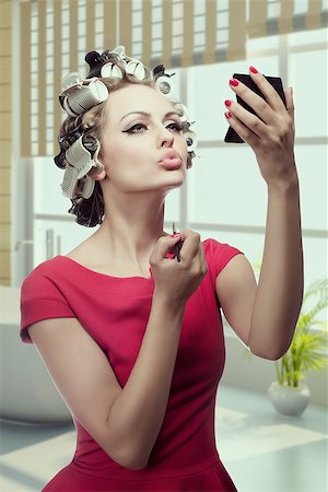 sensual girl applying make-up and looking in the mirror in her hand. Styling her hair with curlers and wearing red dress. Preparing herself for party Stock Photo - Budget Royalty-Free & Subscription, Code: 400-07503850