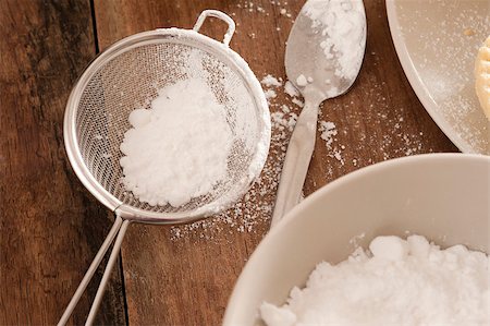 stockarch (artist) - Kitchen sieve filled with icing sugar lying on a wooden kitchen counter alongside a mixing bowl while baking or cooking pastries and food Foto de stock - Royalty-Free Super Valor e Assinatura, Número: 400-07503891
