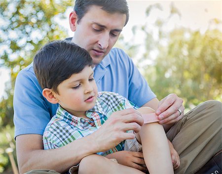 Loving Father Puts a Bandage on the Knee of His Young Son in the Park. Photographie de stock - Aubaine LD & Abonnement, Code: 400-07546055