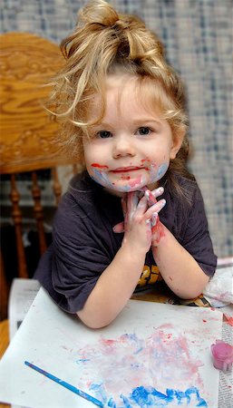 Adorable little girl poses besides her masterpiece.  She has paint smeared on her face and hands. Foto de stock - Royalty-Free Super Valor e Assinatura, Número: 400-07554590