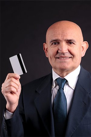 an old businessman with a credit card and a mobile hphone making purchases online; DARK BACKGROUND Stock Photo - Budget Royalty-Free & Subscription, Code: 400-07574956