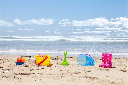 Brightly colored plastic beach toys on the beach with the ocean and clouds in background Foto de stock - Super Valor sin royalties y Suscripción, Código: 400-07578617