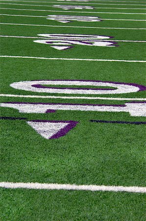 Lines mark off yards of green turf on high school football field.  Numbers ten and twenty are outlined in white and purpe. Foto de stock - Royalty-Free Super Valor e Assinatura, Número: 400-07571772