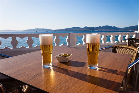 photojope (artist) - Two cold beer glasses and a plate of olives in a table of a terrace next to the sea in Spain. Fotografie stock - Microstock e Abbonamento, Codice: 400-07573355