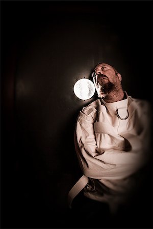 Photo of an insane man in his forties wearing a straitjacket standing in a cell of an asylum with the light from the hallway streaming in. Photographie de stock - Aubaine LD & Abonnement, Code: 400-07580793