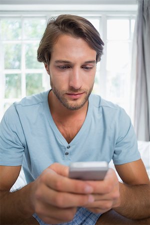 Handsome man sitting on bed sending a text message at home in the living room Stock Photo - Budget Royalty-Free & Subscription, Code: 400-07581932
