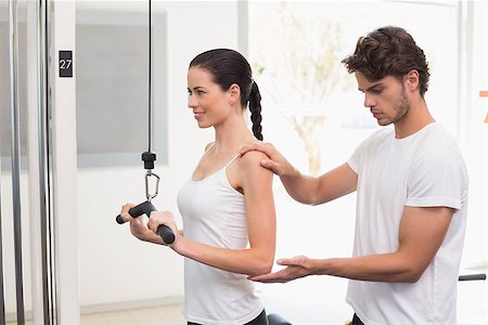 Fit smiling woman using weights machine for arms with her trainer at the gym Foto de stock - Super Valor sin royalties y Suscripción, Código: 400-07583174