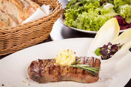 Tasty grilled beef steak topped with a twirled knob of butter and a sprig of fresh rosemary and served on a white plate, close up view Foto de stock - Super Valor sin royalties y Suscripción, Código: 400-07629993