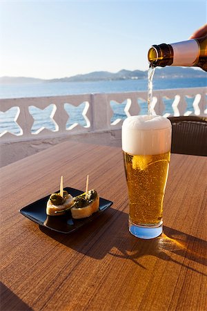 photojope (artist) - Pouring cold beer from the bottle in a glass and a plate of green peppers in the table of a terrace next to the sea in Spain. Photographie de stock - Aubaine LD & Abonnement, Code: 400-07632780