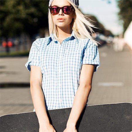 simsearch:400-07506274,k - Young blond girl with plump lips in sunglasses stands in the street on sunny day holding skateboard with two hands Fotografie stock - Microstock e Abbonamento, Codice: 400-07659110