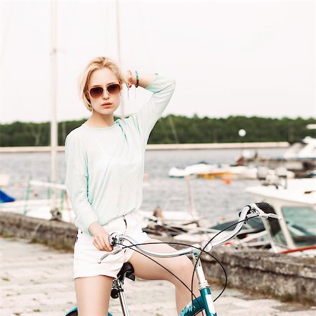 beautiful blond girl in light summer style on city bike adjusts her hair at sea pier against yachts Stock Photo - Budget Royalty-Free & Subscription, Code: 400-07659144