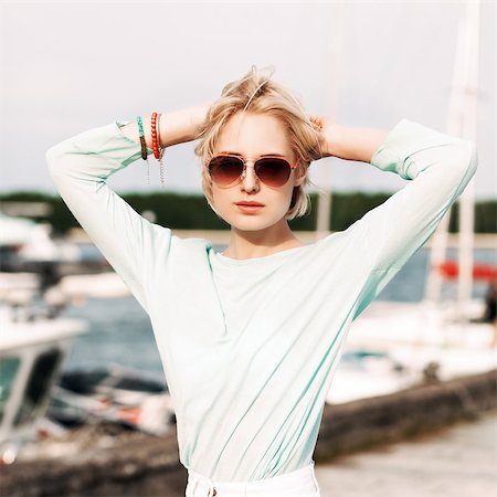 beautiful blond girl in light summer style on city bike keeps her hands behind head at sea pier against yachts Stock Photo - Budget Royalty-Free & Subscription, Code: 400-07659145