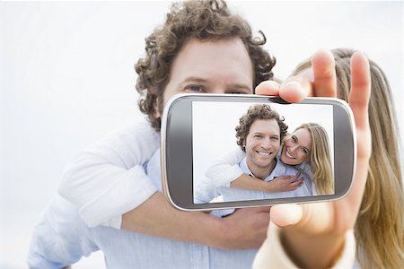 simsearch:400-07664794,k - Hand holding smartphone showing man piggybacking woman at beach Stock Photo - Budget Royalty-Free & Subscription, Code: 400-07664808