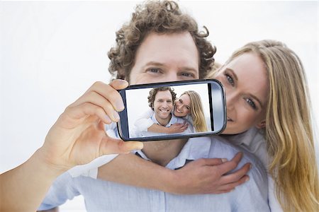 simsearch:400-07664794,k - Hand holding smartphone showing man piggybacking woman at beach Stock Photo - Budget Royalty-Free & Subscription, Code: 400-07664819