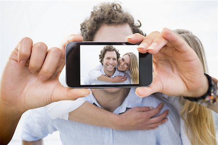 simsearch:400-07664794,k - Hand holding smartphone showing man piggybacking woman at beach Stock Photo - Budget Royalty-Free & Subscription, Code: 400-07664827