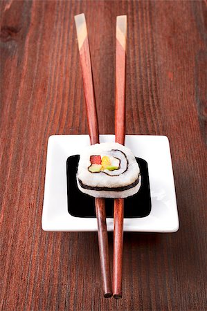 simsearch:689-03123940,k - Maki sushi on chopsticks on soy sauce in white bowl on dark wooden background. Photographie de stock - Aubaine LD & Abonnement, Code: 400-07667128