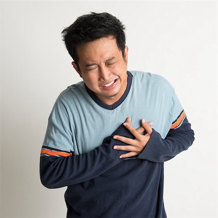Asian male heartache, pressing on chest with painful expression, on plain background Stock Photo - Budget Royalty-Free & Subscription, Code: 400-07667608