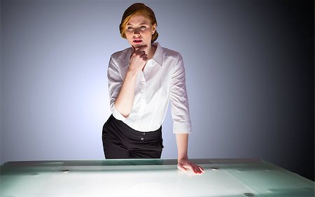 simsearch:400-04035704,k - Redhead businesswoman standing and thinking by a desk on shadow background Fotografie stock - Microstock e Abbonamento, Codice: 400-07663488