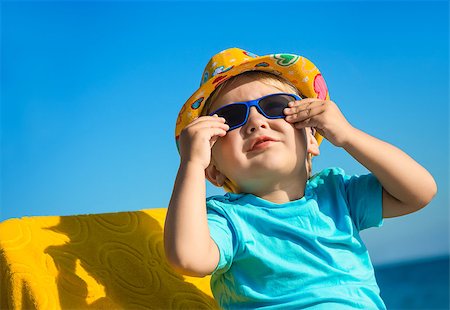 Boy kid in sun glasses and hat on beach against blue sky Stock Photo - Budget Royalty-Free & Subscription, Code: 400-07676952