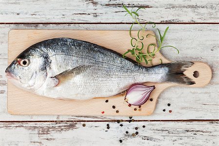 simsearch:400-07776969,k - Delicious fresh sea bream fish on wooden kitchen board with onion, rosemary and colorful peppercorns on white textured wooden background. Culinary healthy cooking. Foto de stock - Super Valor sin royalties y Suscripción, Código: 400-07677162