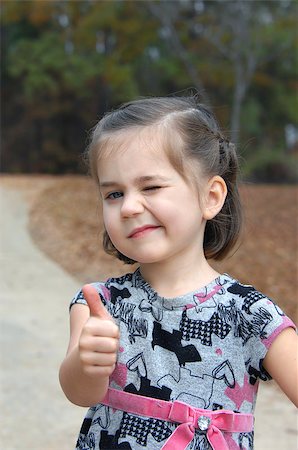 Little girl gives a "thumbs up" sign and winks.  She is playing outside and is enjoying the great outdoors. Foto de stock - Royalty-Free Super Valor e Assinatura, Número: 400-07678020