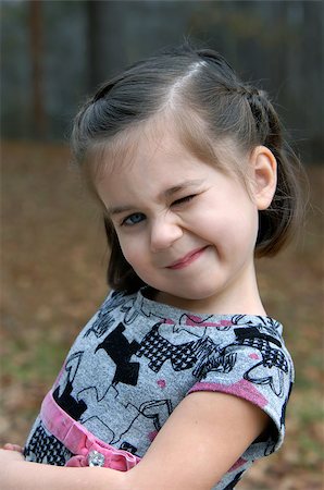 Cute little girl tilts her head and winks.  She is outdoors and is wearing a grey and pink print dress. Foto de stock - Royalty-Free Super Valor e Assinatura, Número: 400-07678022