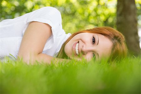 Pretty redhead smiling at camera lying on the grass on a sunny day Photographie de stock - Aubaine LD & Abonnement, Code: 400-07684326