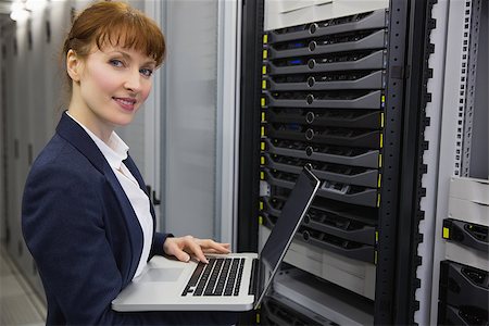 Pretty technician using laptop while working on server smiling at camera in large data center Stock Photo - Budget Royalty-Free & Subscription, Code: 400-07684416