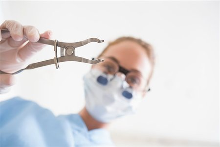 female with dental tools at work - Dentist in surgical mask and dental loupes holding pliers over patient at the dental clinic Stock Photo - Budget Royalty-Free & Subscription, Code: 400-07685088