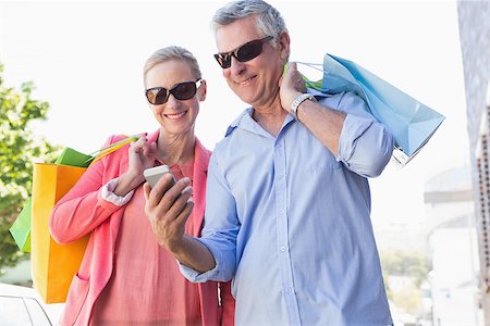 Happy senior couple looking at smartphone holding shopping bags on a sunny day Stock Photo - Budget Royalty-Free & Subscription, Code: 400-07685792