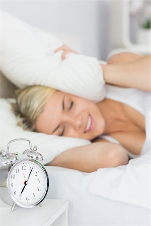 Woman covering ears with pillow in bed and alarm clock on side table Stock Photo - Budget Royalty-Free & Subscription, Code: 400-07687168