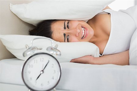 Woman covering ears with pillows in bed and alarm clock on side table Stock Photo - Budget Royalty-Free & Subscription, Code: 400-07687196