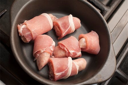 stockarch (artist) - Cooking pigs in blankets, or rashers of bacon wrapped around beef and pork sausages, with a batch of uncooked piggies in a cast iron casserole dish waiting to be cooked in the oven or on a hot griddle Stock Photo - Budget Royalty-Free & Subscription, Code: 400-07682402