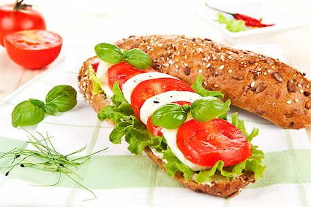 Wholegrain baguette with fresh mozzarella, tomatoes, lettuce and basil on kitchen towel. Stock Photo - Budget Royalty-Free & Subscription, Code: 400-07715751