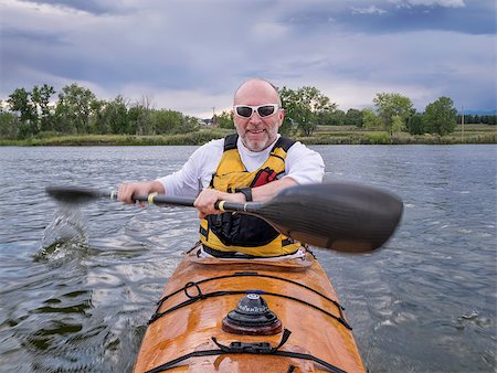 simsearch:400-07795226,k - a bow view of a senior male paddling a home-built wooden sea kayak on a lake in Colorado, focus on face with arms and paddle in a motion blur Foto de stock - Royalty-Free Super Valor e Assinatura, Número: 400-07718851