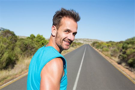 simsearch:400-07725266,k - Fit man jogging on the open road smiling at camera on a sunny day Photographie de stock - Aubaine LD & Abonnement, Code: 400-07724969