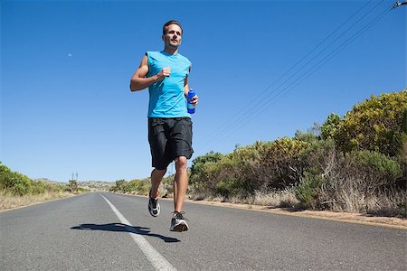 rodovia 40 - Athletic man jogging on open road holding bottle on a sunny day Foto de stock - Royalty-Free Super Valor e Assinatura, Número: 400-07725279