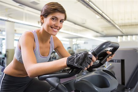 simsearch:400-07725687,k - Fit smiling brunette working out on the exercise bike at the gym Photographie de stock - Aubaine LD & Abonnement, Code: 400-07725679