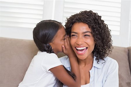 Pretty mother sitting on the couch with her daughter whispering a secret at home in the living room Stock Photo - Budget Royalty-Free & Subscription, Code: 400-07726166