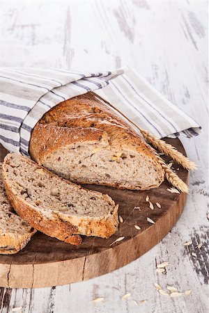 simsearch:400-07996450,k - Whole grain baguette on round wooden kitchen board on white textured wooden background. Culinary bread eating, breakfast concept. Foto de stock - Royalty-Free Super Valor e Assinatura, Número: 400-07745958