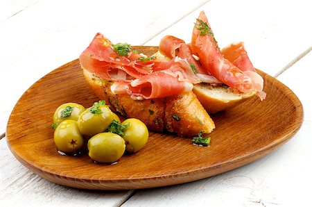 pane all'aglio - Delicious Tapas with Smoked Ham, Garlic Bread and Green Olives on Wooden Plate closeup on White Wooden background Fotografie stock - Microstock e Abbonamento, Codice: 400-07749261