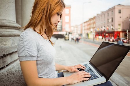 simsearch:400-07778671,k - Focused pretty redhead typing on laptop in the street Fotografie stock - Microstock e Abbonamento, Codice: 400-07778602