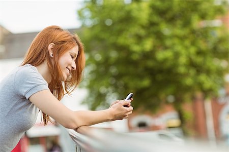 simsearch:400-07778671,k - Cheerful redhead with her mobile phone texting a message in the city Fotografie stock - Microstock e Abbonamento, Codice: 400-07778637
