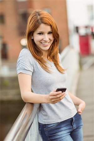 simsearch:400-07778671,k - Smiling redhead with her mobile phone texting a message in the city Fotografie stock - Microstock e Abbonamento, Codice: 400-07778643